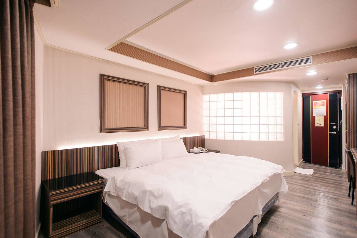 Habitación de hotel con una cama grande, una mesita de noche y una puerta con un cartel.