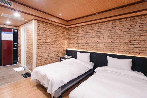 A hotel room with two beds, a brick wall, wooden ceiling, and a door with a sign.