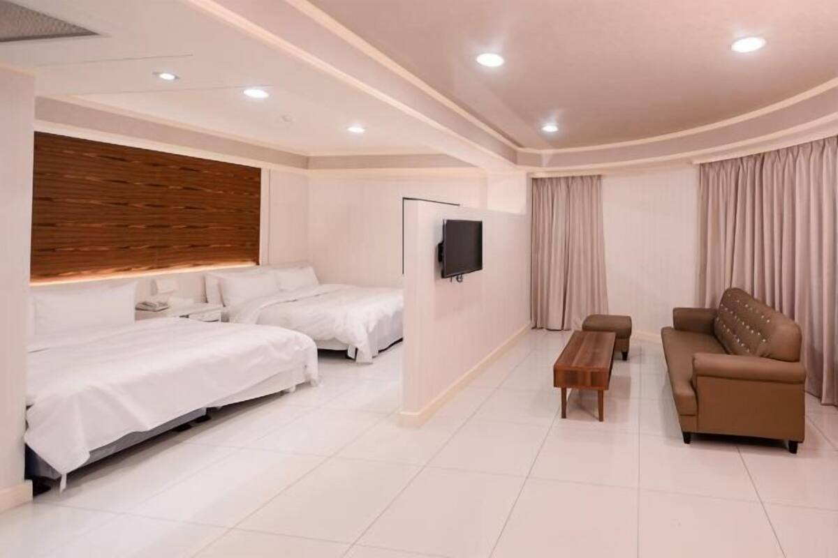 Una habitación de hotel con dos camas, un sofá, un televisor y un cabecero de madera.