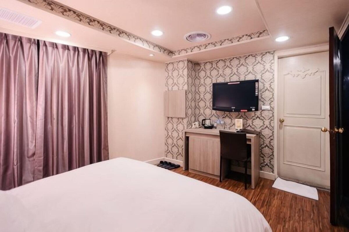 A hotel room with a bed, a desk with a computer, a television, and a door.
