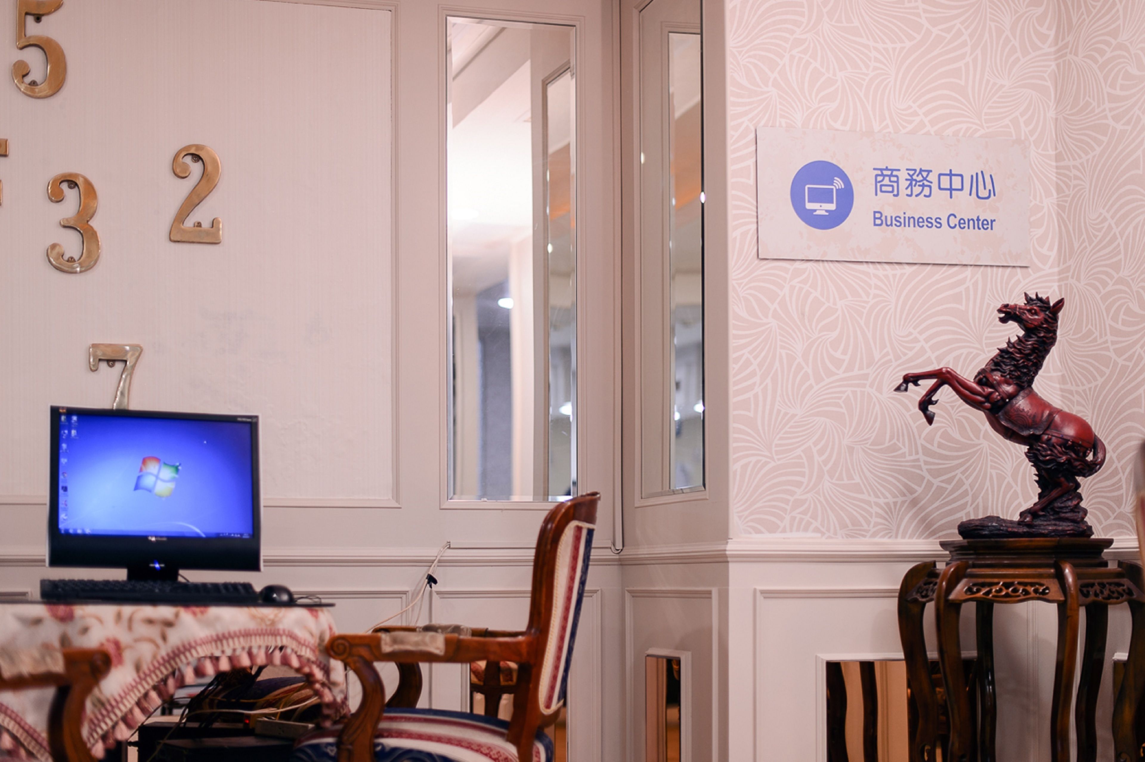 A room with a computer on a desk, a chair, a decorative horse statue, and a sign indicating a business center.
