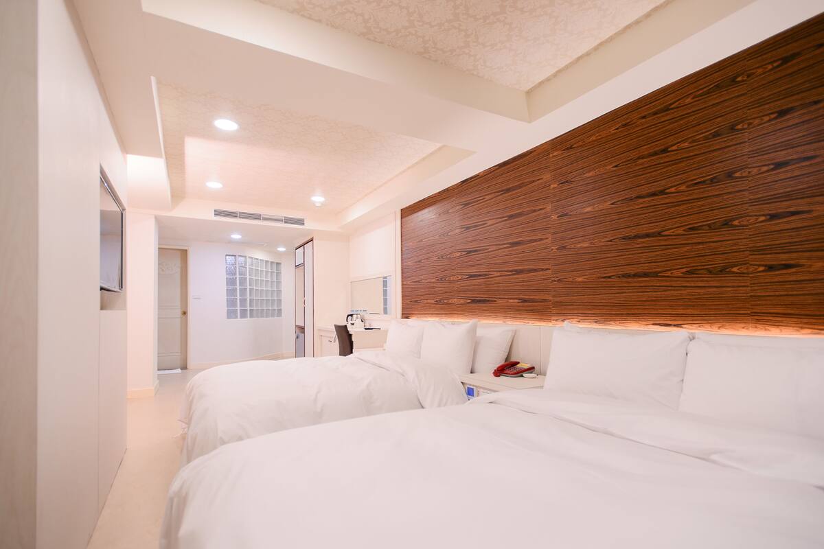 Una habitación de hotel moderna con dos camas, un cabecero de madera, una mesita de noche y un escritorio pequeño con una silla.