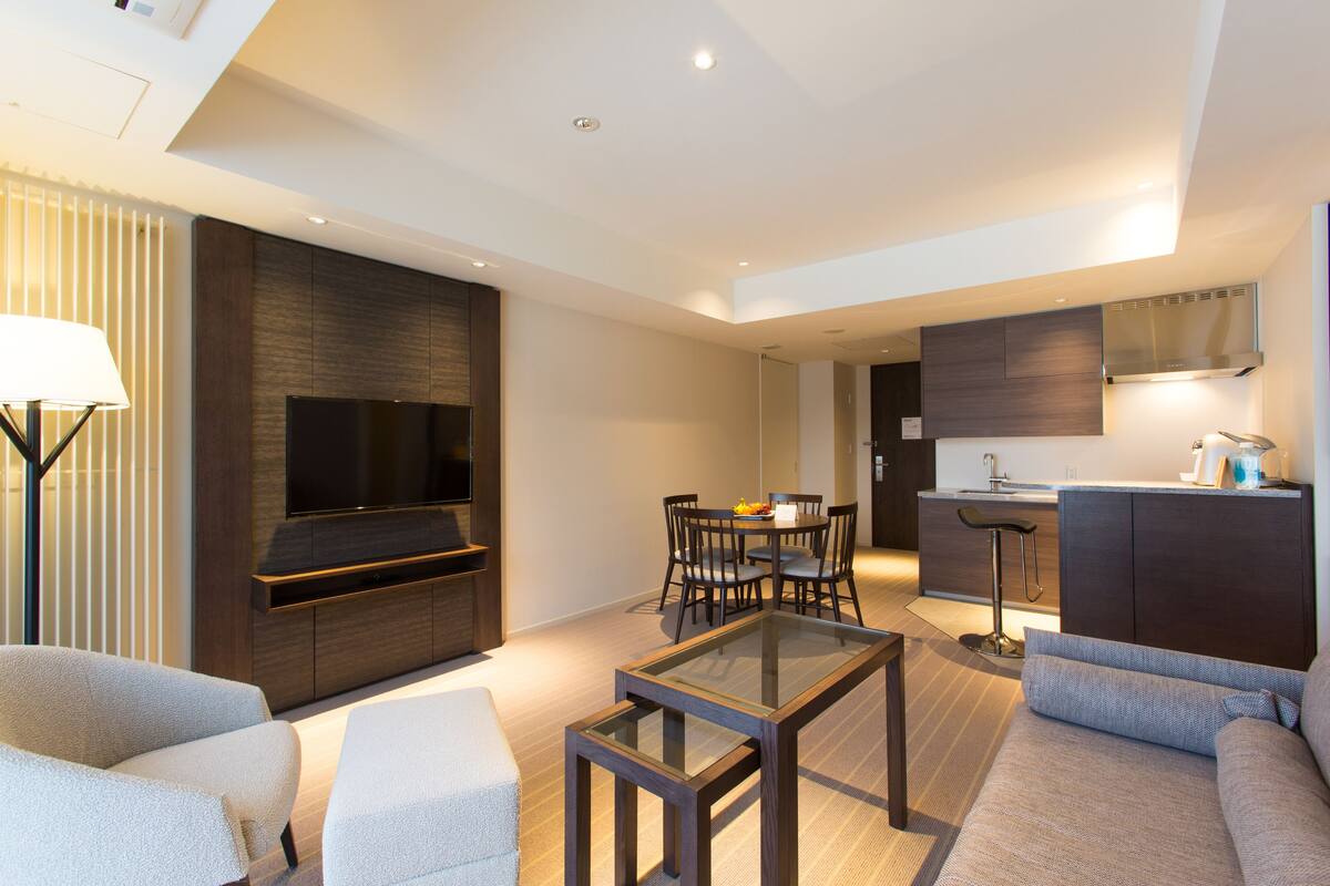 A modern living room with a glass coffee table, a sofa, and a TV mounted on the wall.