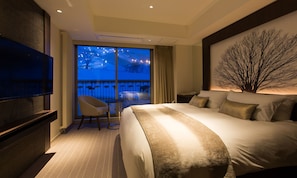 Une chambre d’hôtel avec un grand lit, une télévision, un fauteuil et un balcon donnant sur un paysage enneigé.