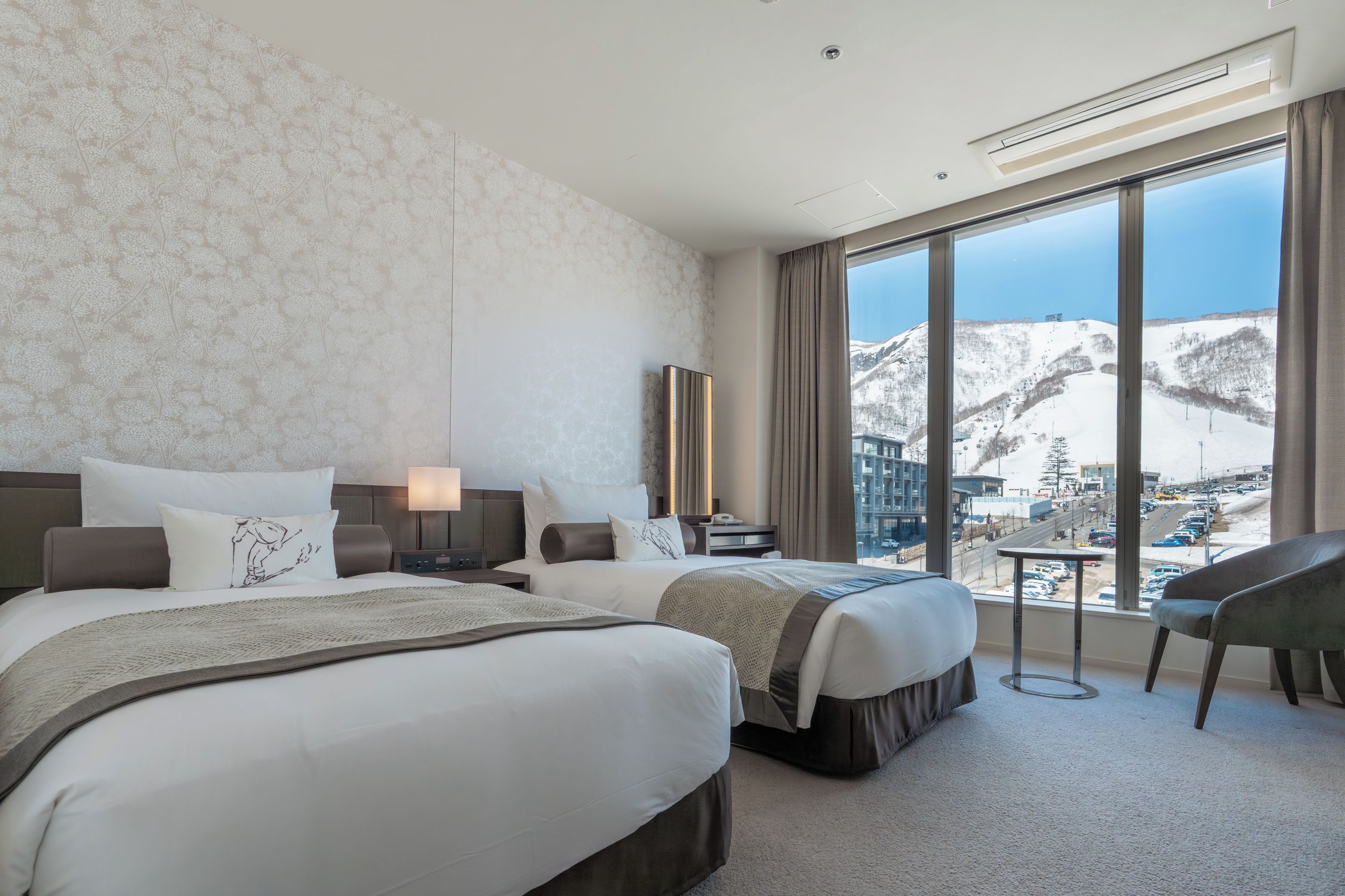 A hotel room with two beds, a large window with a mountain view, and a chair.