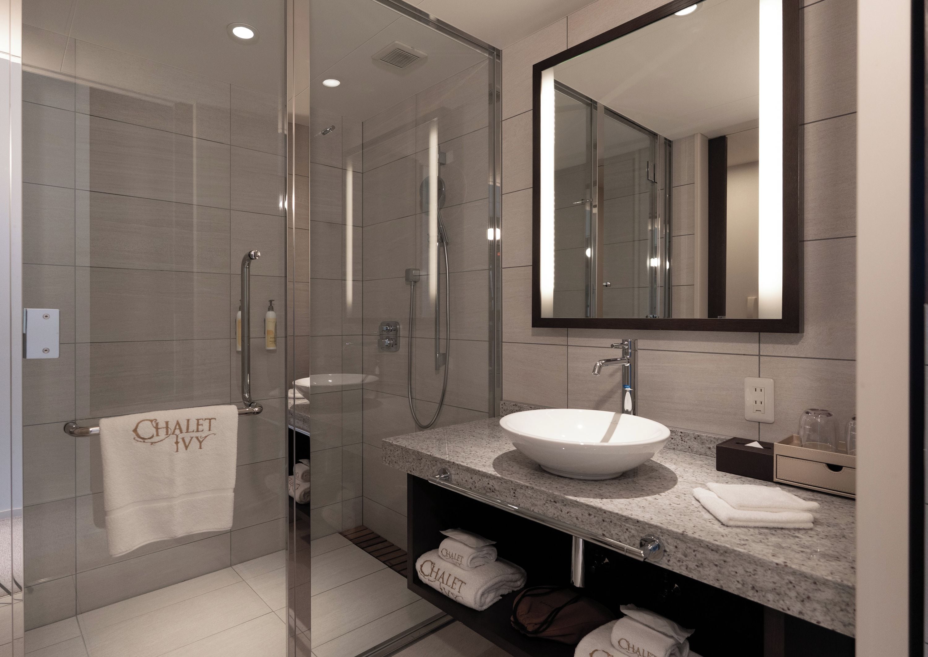 A modern bathroom with a glass-enclosed shower, a large mirror, and a granite countertop sink.