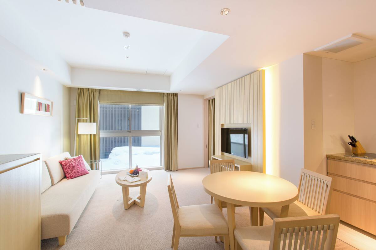 A modern hotel room with a sofa, a round dining table, and a TV.
