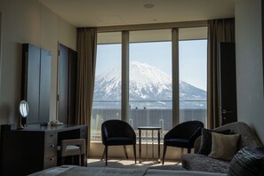 A hotel room with a bed, a desk, a chair, a small table, and a view of a mountain. - Chalet Ivy Hirafu (Kutchan)