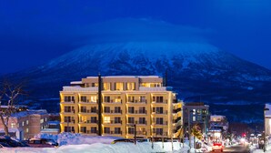 A multi-story hotel with balconies, a snow-covered street, and a mountain in the background. - Chalet Ivy Hirafu (Kutchan)