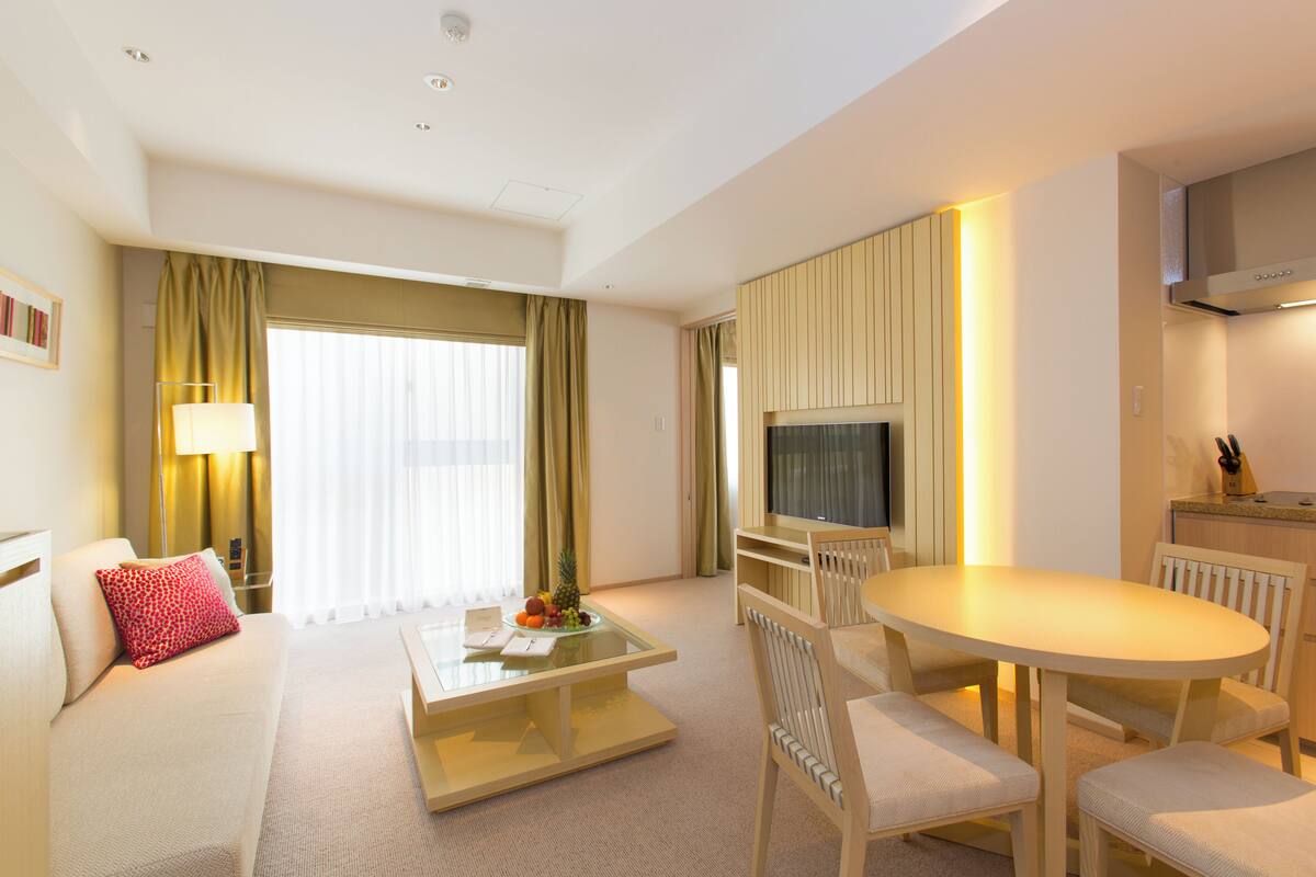 A modern hotel room with a sofa, a coffee table, a TV, and a dining area.