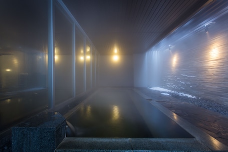 A modern indoor pool area with clear glass walls, a wooden floor, and a stone ledge.