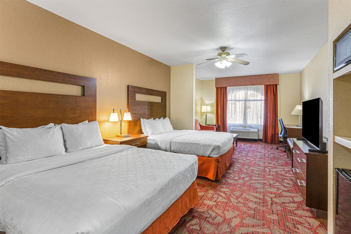 A hotel room with two beds, a ceiling fan, a TV, and a desk with a lamp.