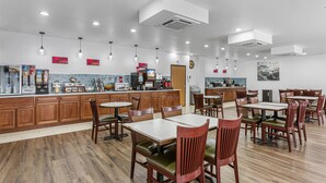 Un restaurant moderne avec des meubles en bois, de nombreuses tables et chaises, et une cuisine visible au fond de la salle.