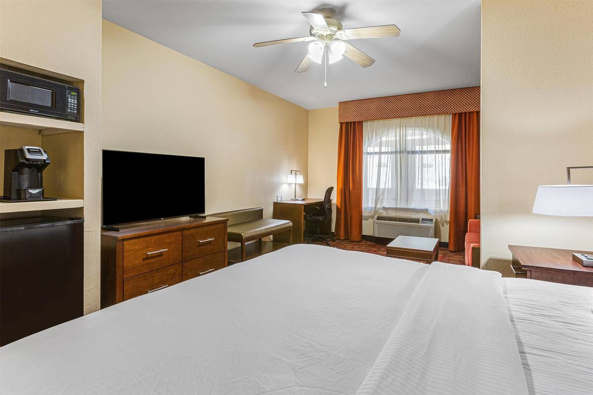 A hotel room with a bed, a desk, a television, a coffee machine, and a ceiling fan.