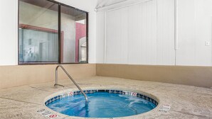 Une piscine intérieure avec un escalier en métal, entourée d’un sol beige et de murs blancs.