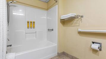 Un baño con una bañera blanca, ducha y toallero con toallas. Hay tres botellas amarillas en la pared.