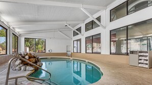 Une piscine intérieure avec des parois en verre transparent, un sol carrelé en pierre et un escalier en métal.