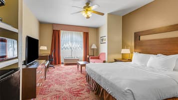 Quarto de hotel com cama, escrivaninha, televisão, cadeira e ventilador de teto.
