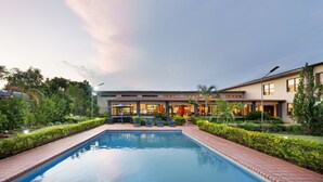 A modern hotel with a swimming pool, well-maintained gardens, and a clear sky.