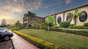 A modern building with a parking area, neatly trimmed hedges, and palm trees.