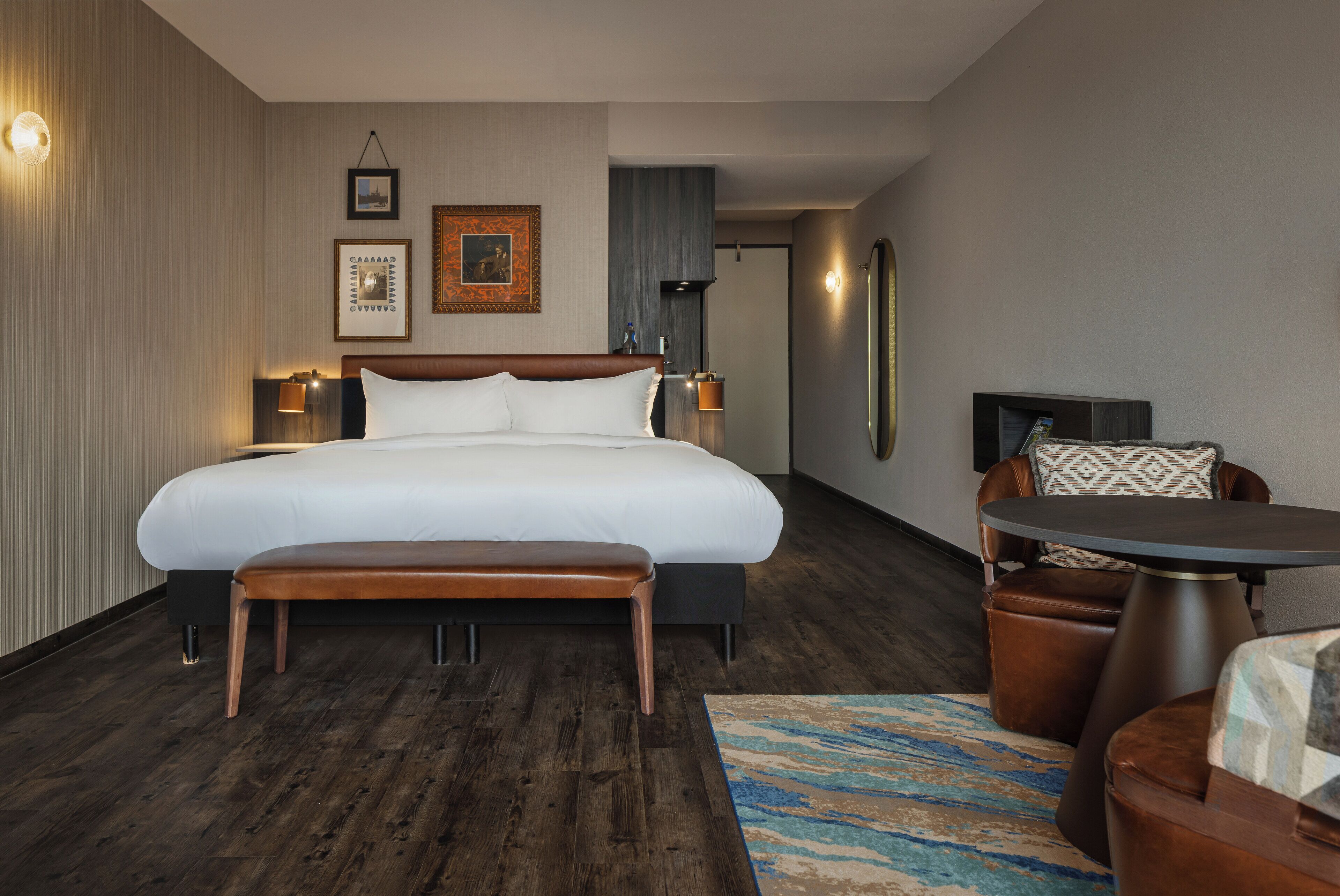 Een moderne hotelkamer met een groot bed, een klein rond tafeltje en een bankje.