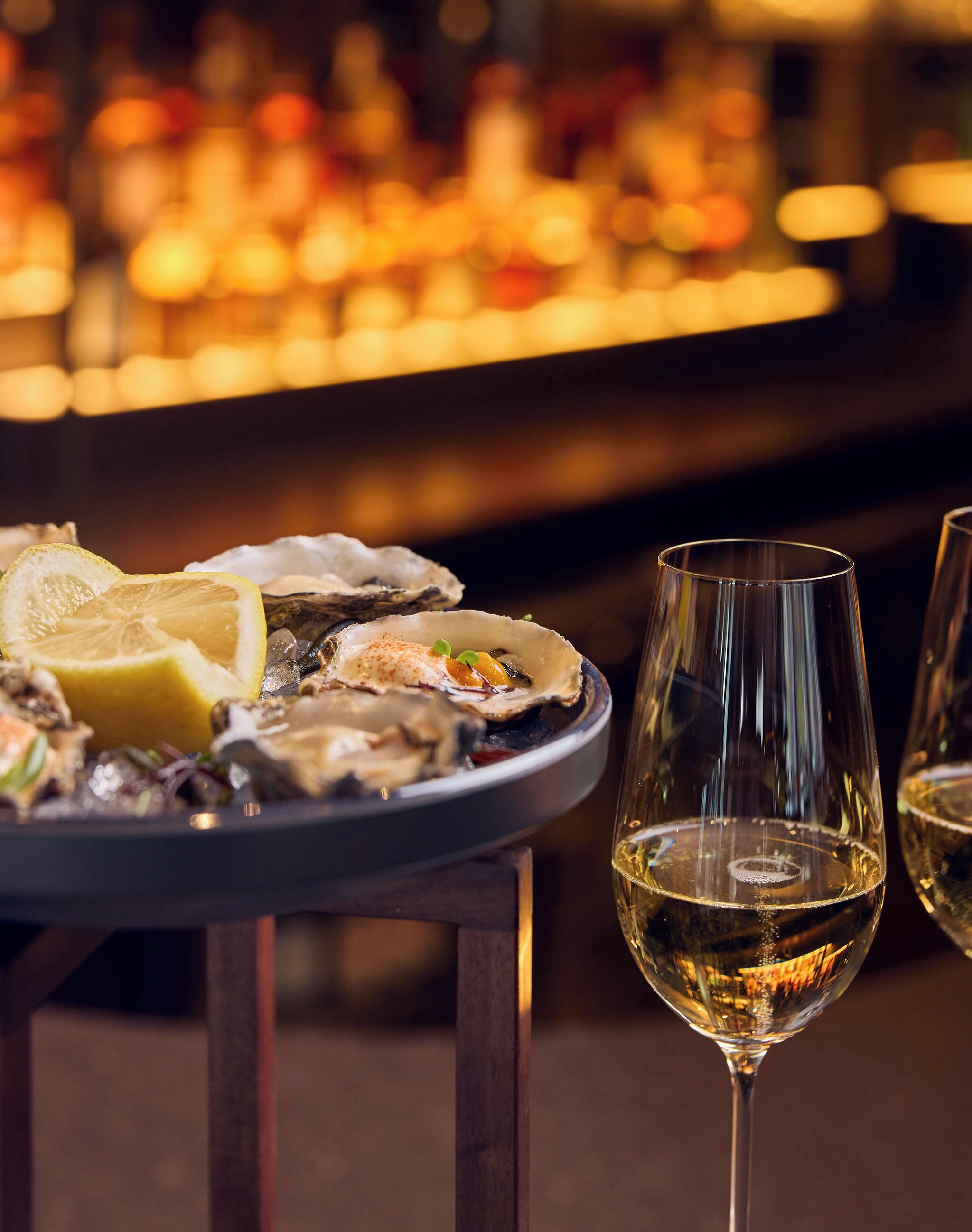 Een barscène met oesters op ijs, een partje citroen en een glas witte wijn.