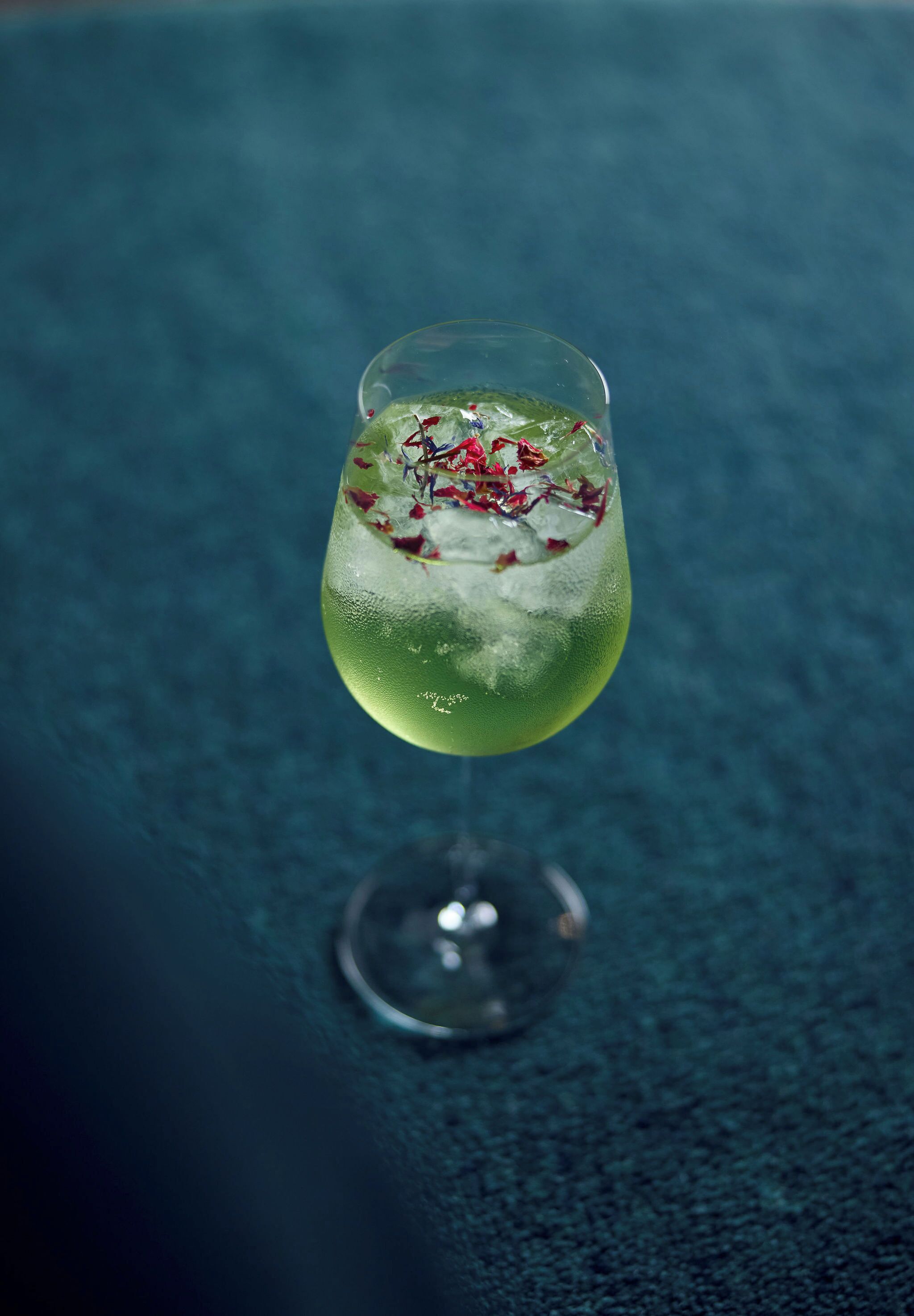 Um cocktail num copo com haste, gelo e guarnições sobre uma superfície texturizada.
