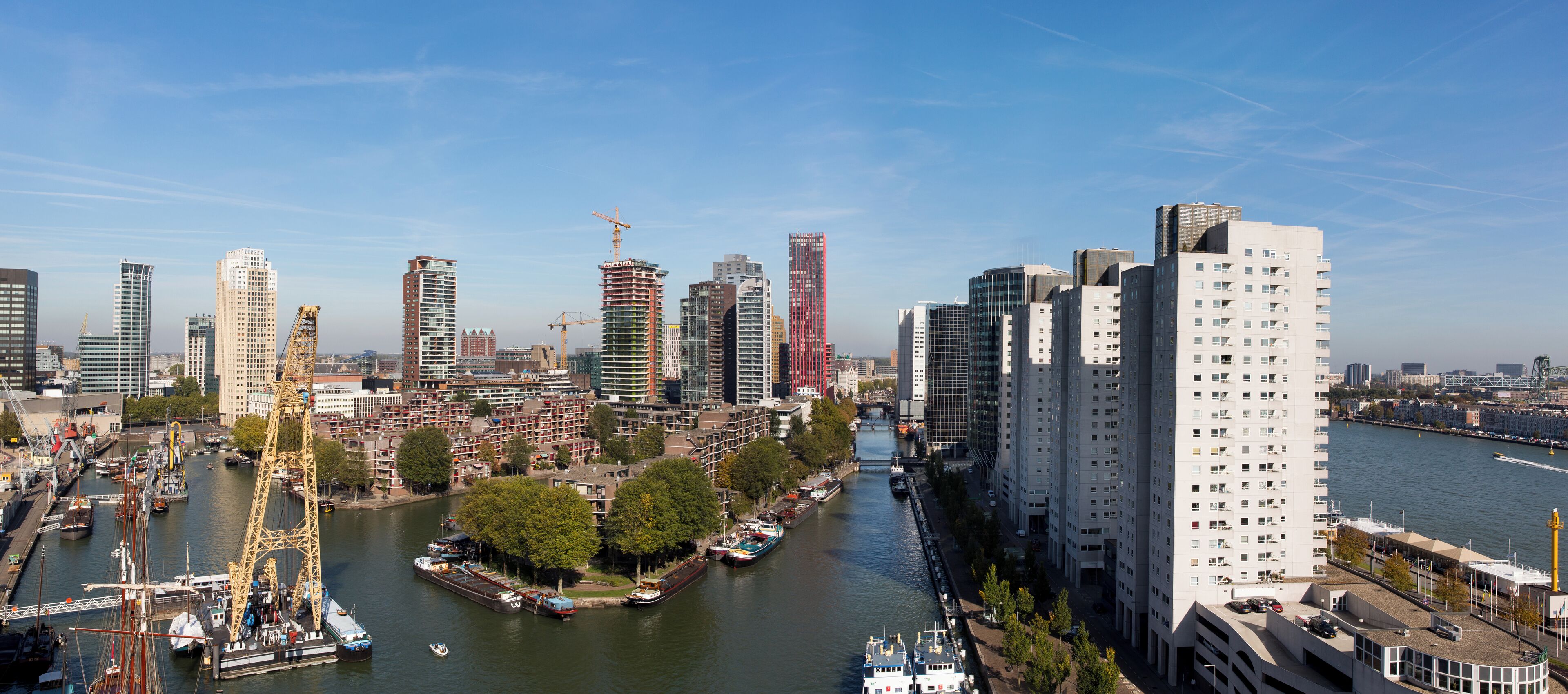 A high-rise building with a modern architectural design, situated next to a river with boats docked along the waterfront.