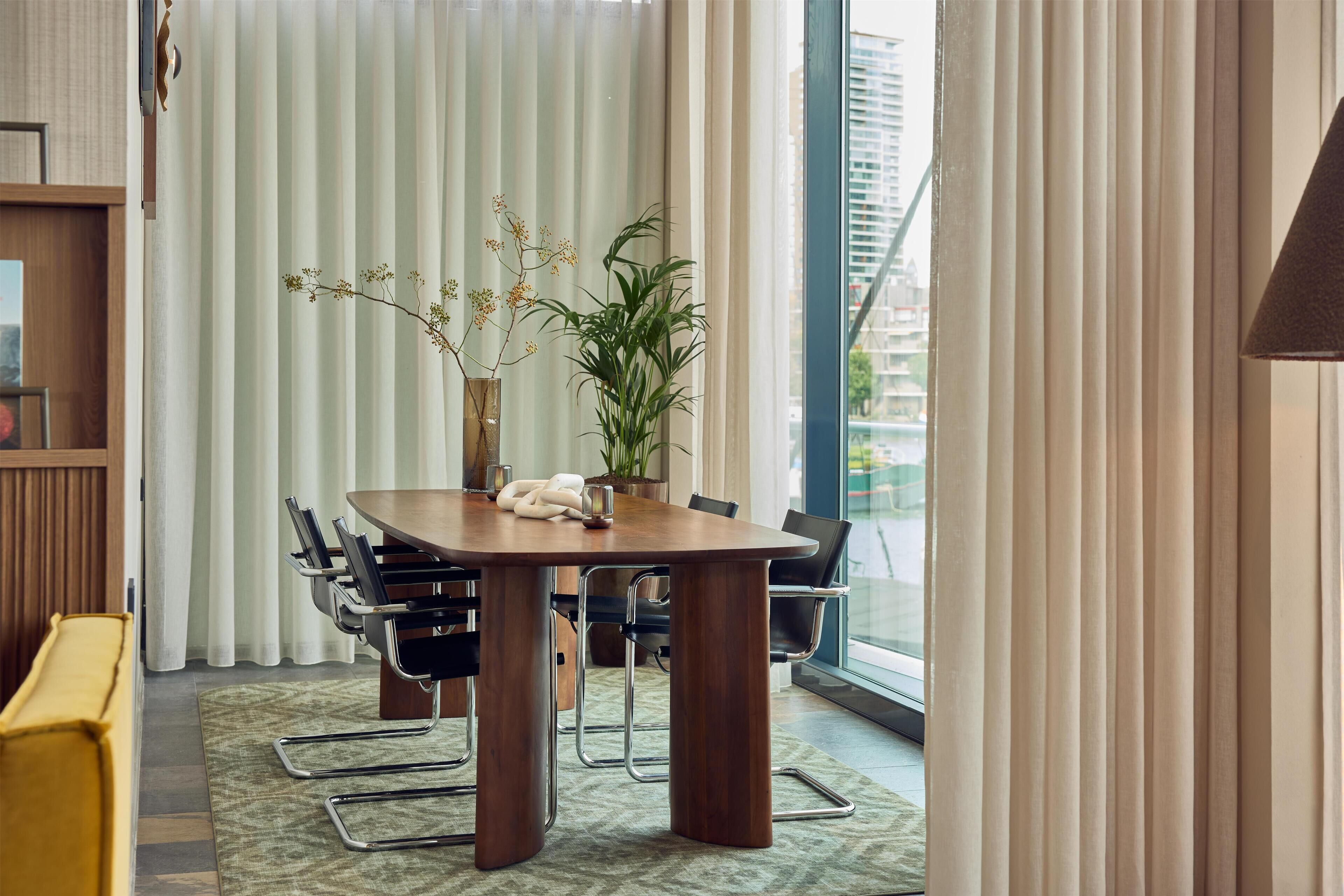 Een moderne vergaderruimte met een houten tafel, zwarte stoelen, een potplant en uitzicht op een stadsgezicht door grote ramen.