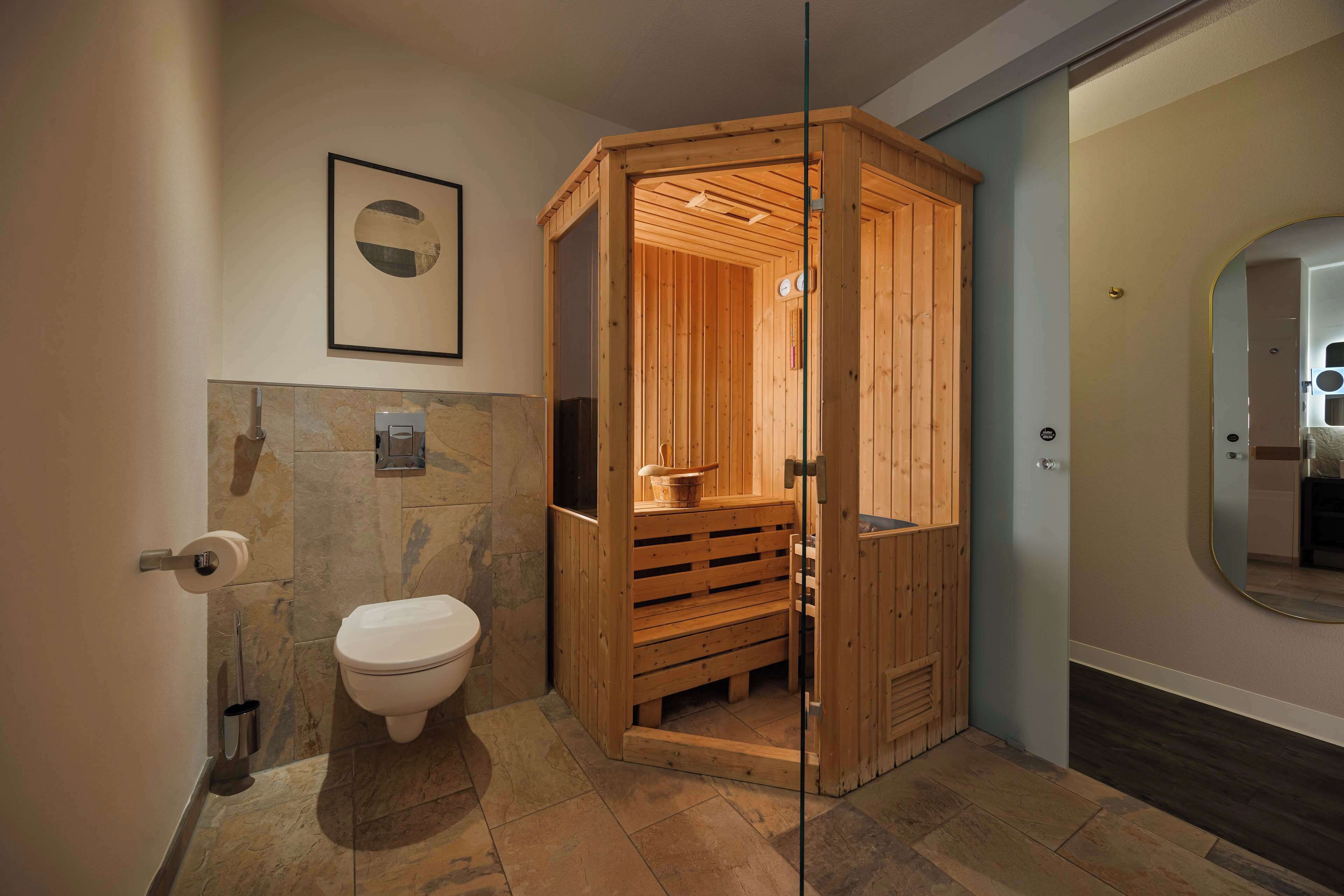 Un baño moderno con sauna de madera, inodoro y suelo de baldosas de mármol.