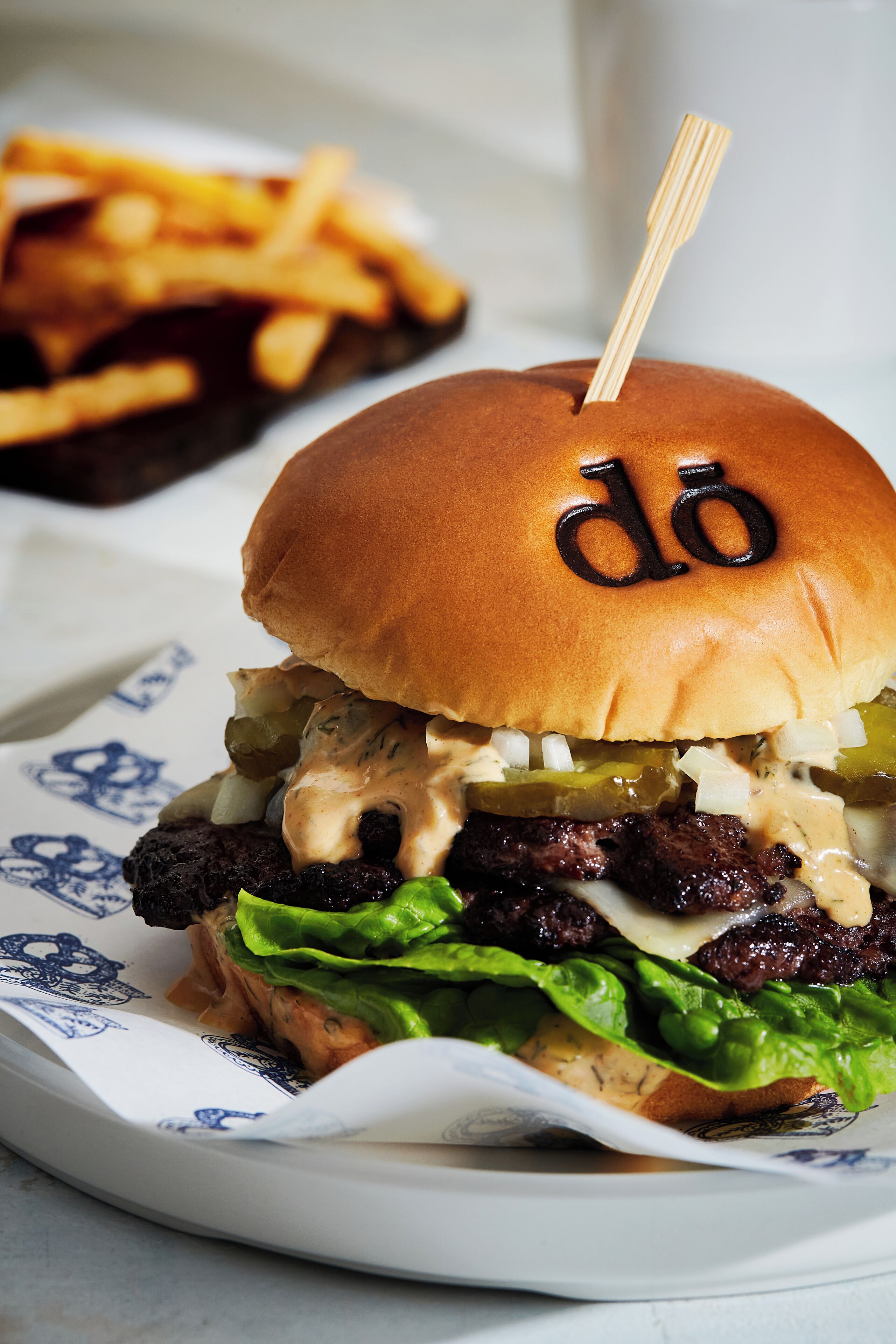Un hamburger avec un cure-dent en bois planté dans le pain, de la laitue, des cornichons et une sauce crémeuse.