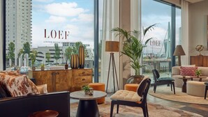 A modern living room with a large window, a wooden cabinet, a sofa, a chair, and a coffee table. - Haven Hotel Rotterdam, Curio Collection by Hilton (Rotterdam)