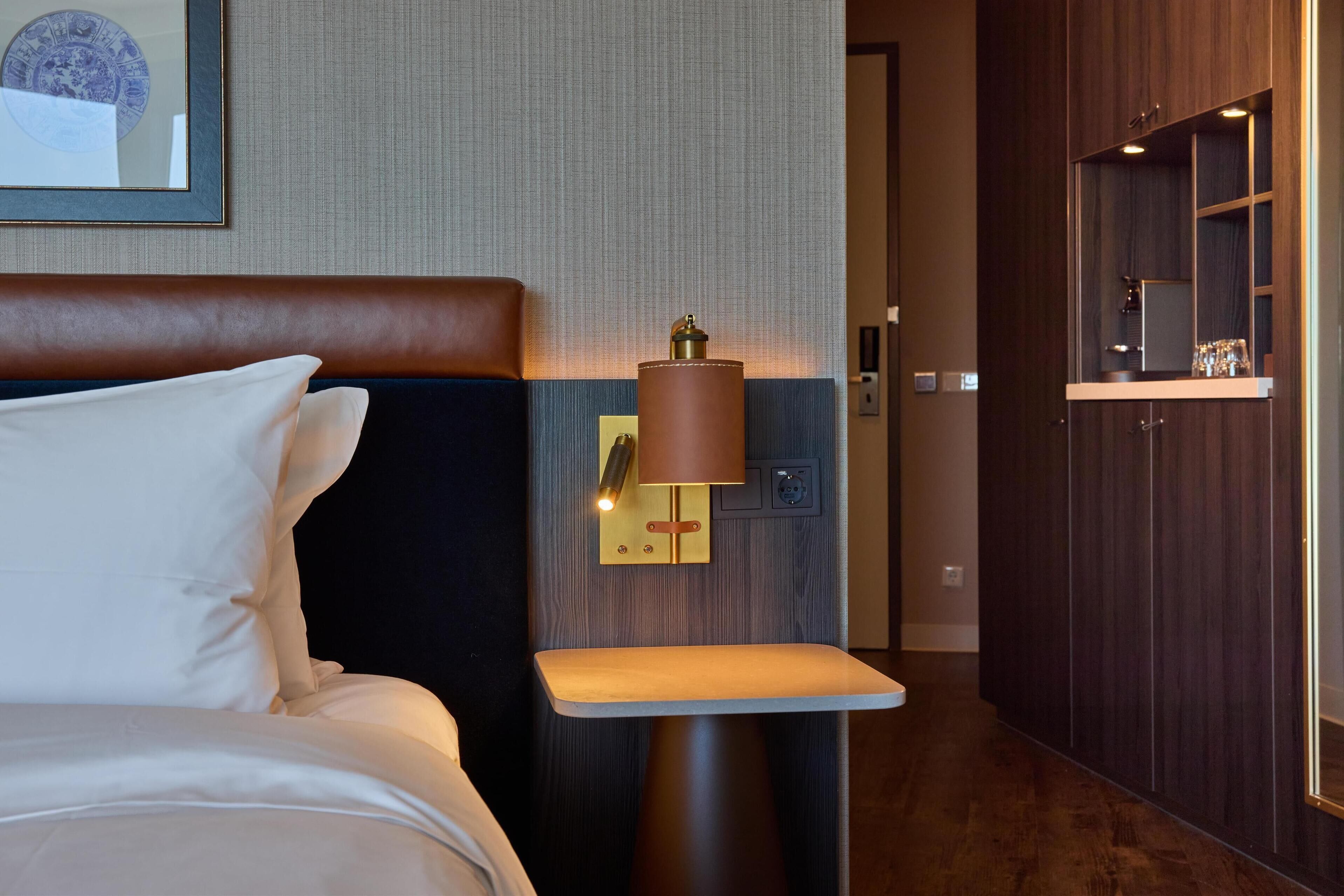 Habitación de hotel con cama, mesita de noche con lámpara, una pequeña mesa y pared de paneles de madera.