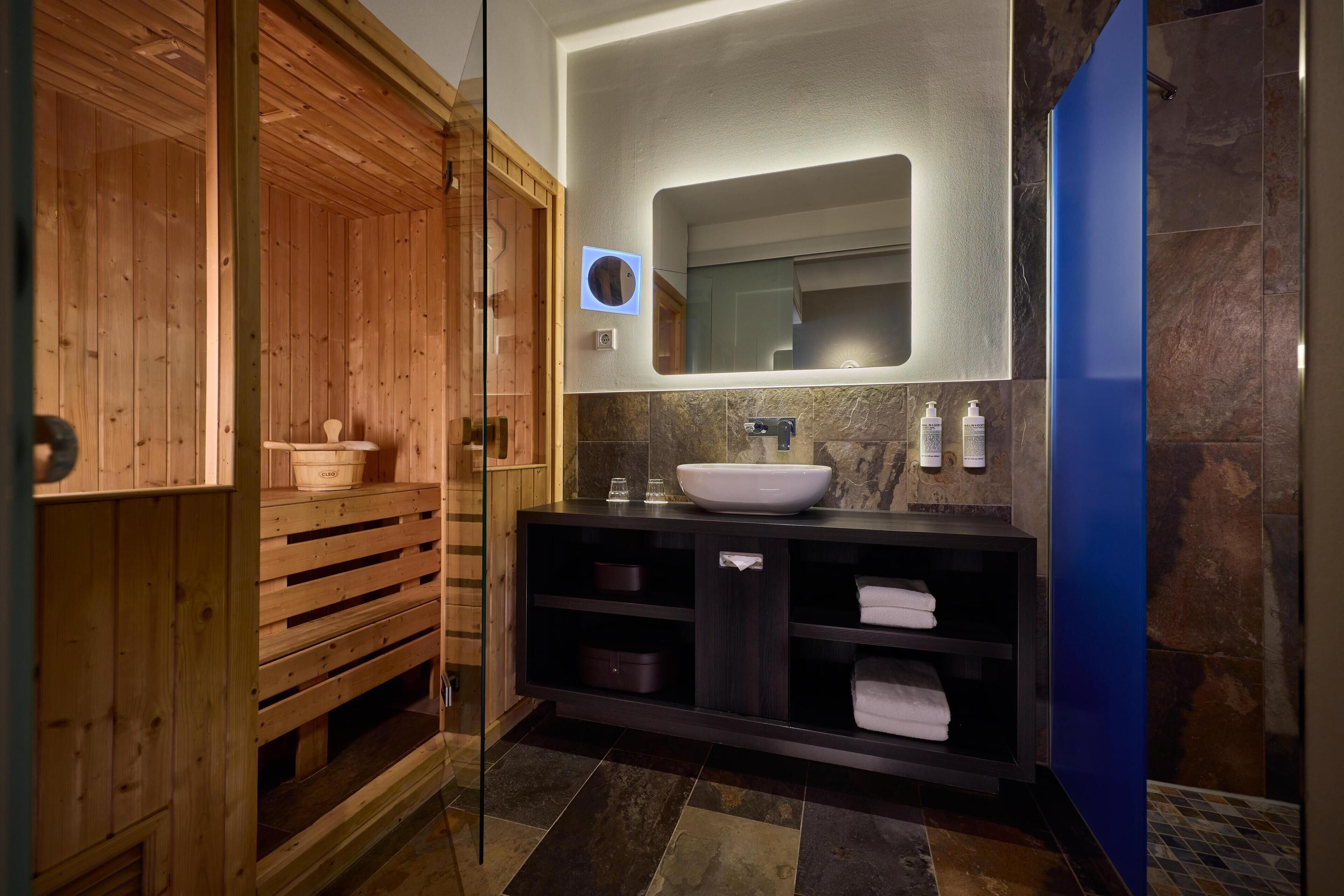 Un baño moderno con sauna de madera, un lavamanos grande con encimera de mármol y una pared decorada en azul.