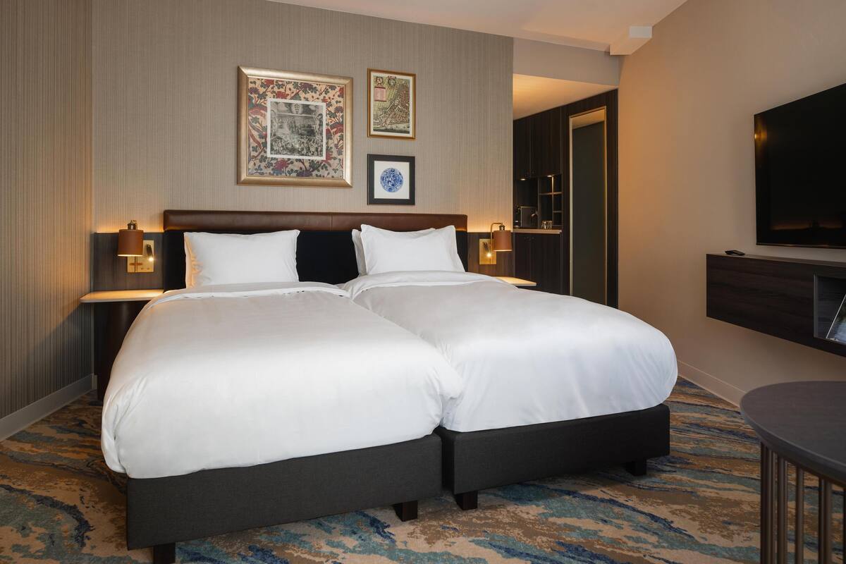 A double bed with white linens, two bedside tables with lamps, a flat-screen TV, and framed artwork on the wall.