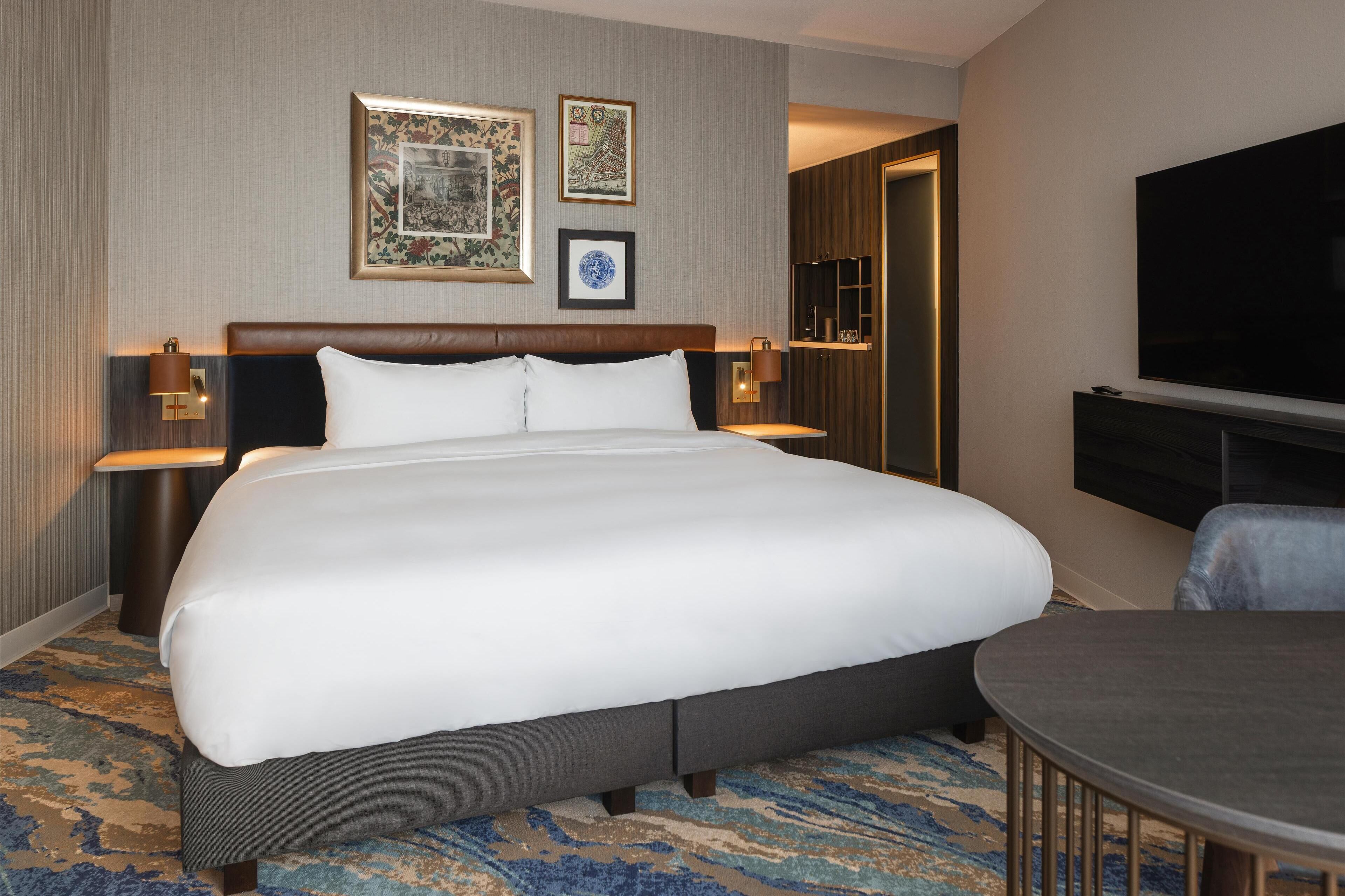 A large bed with a headboard, two wall-mounted lamps, and a flat-screen TV on the wall.
