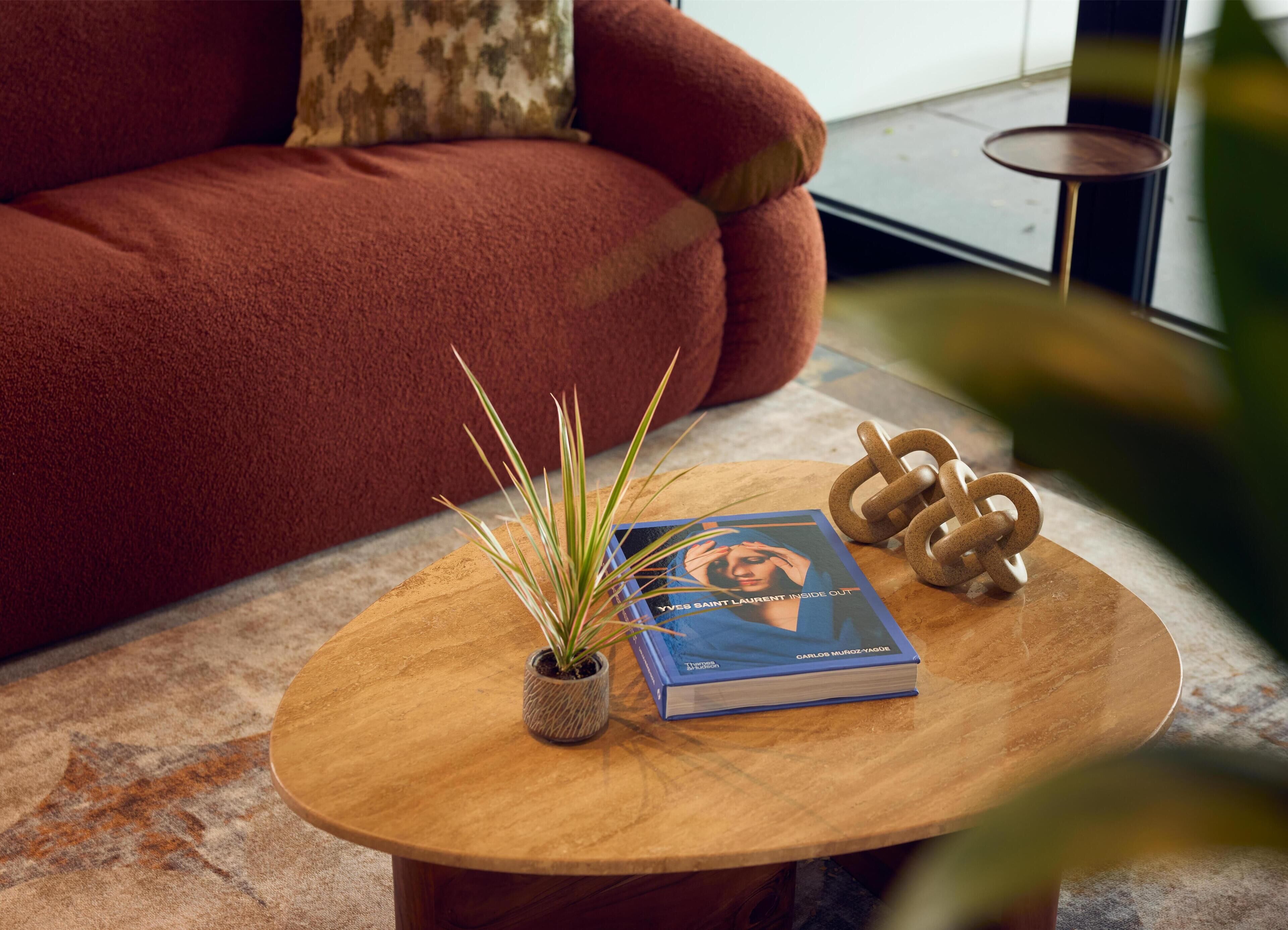 Ein runder Couchtisch aus Holz mit einem Buch mit dem Titel 'Yves Saint Laurent Inside Out' und einer kleinen Topfpflanze.