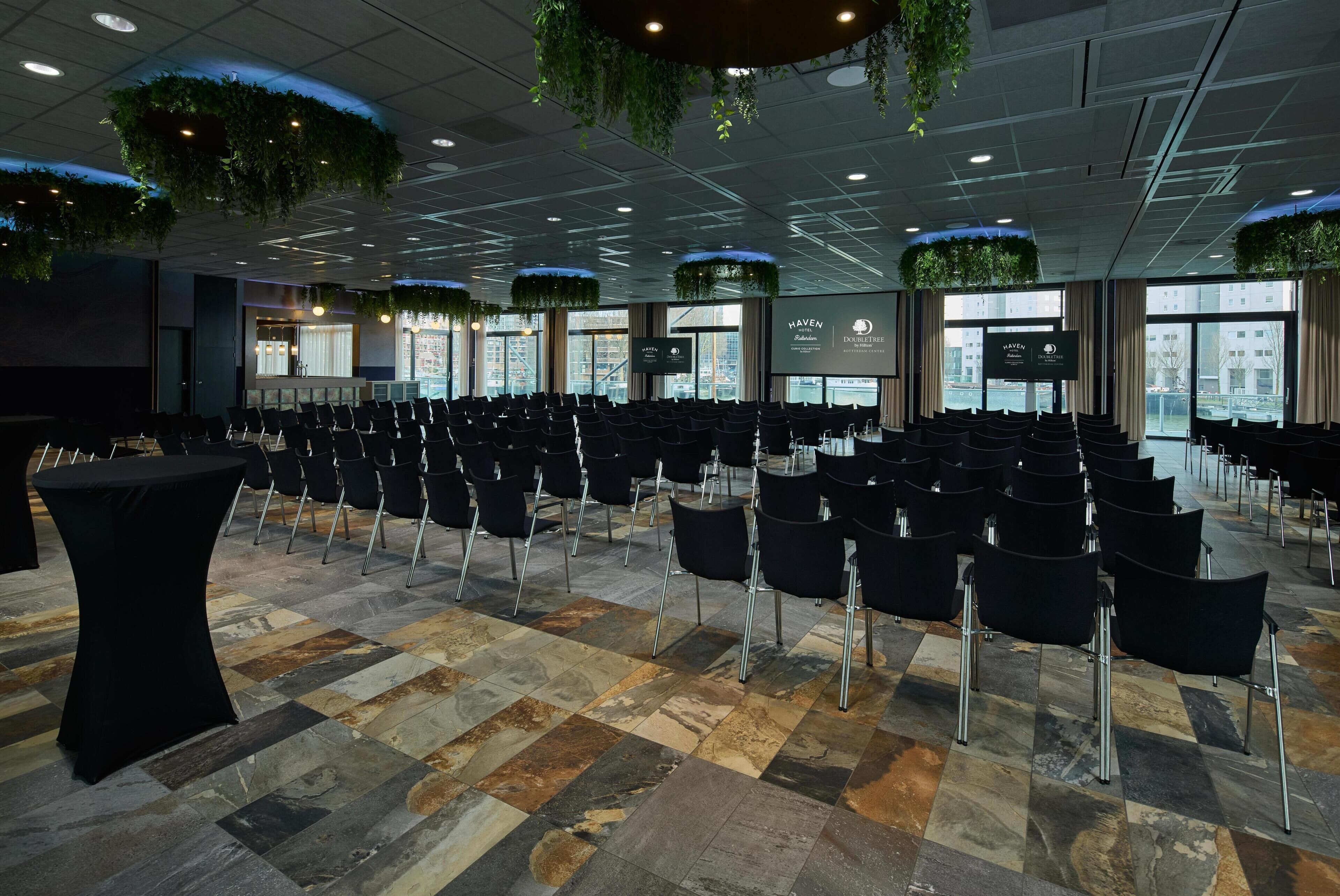 A conference room with rows of chairs, a black table, and hanging plants.