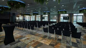 A conference room with rows of chairs, a black table, and hanging plants.