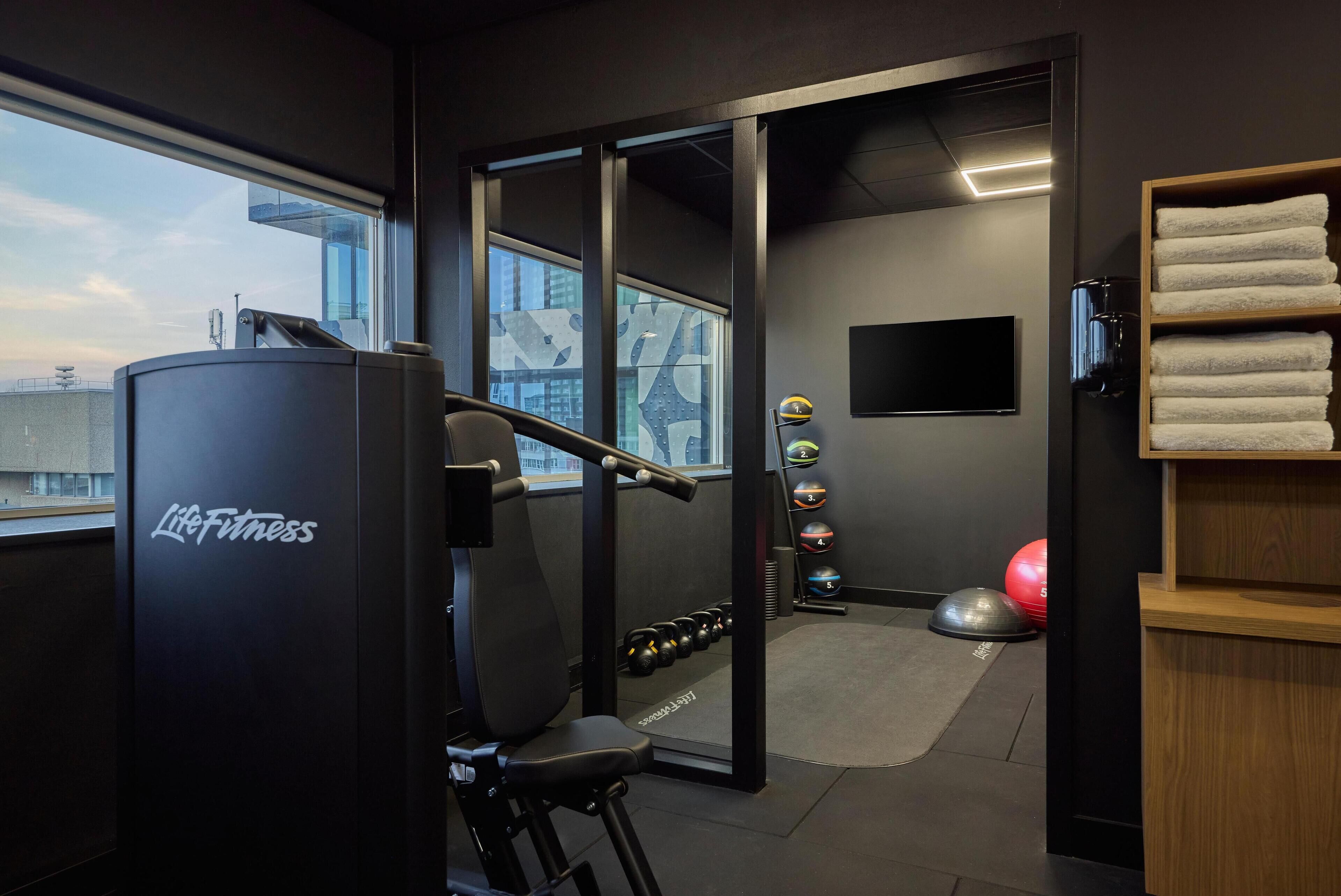 Un gimnasio con bancos de pesas, mancuernas y pelotas de ejercicio.