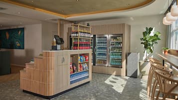 Een moderne bar met een houten toonbank, planken vol snacks en drankjes, en een koelkast.