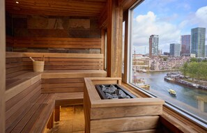 A wooden sauna with benches and a stone firebox, overlooking a river with boats and city buildings. - Haven Hotel Rotterdam, Curio Collection by Hilton (Rotterdam)
