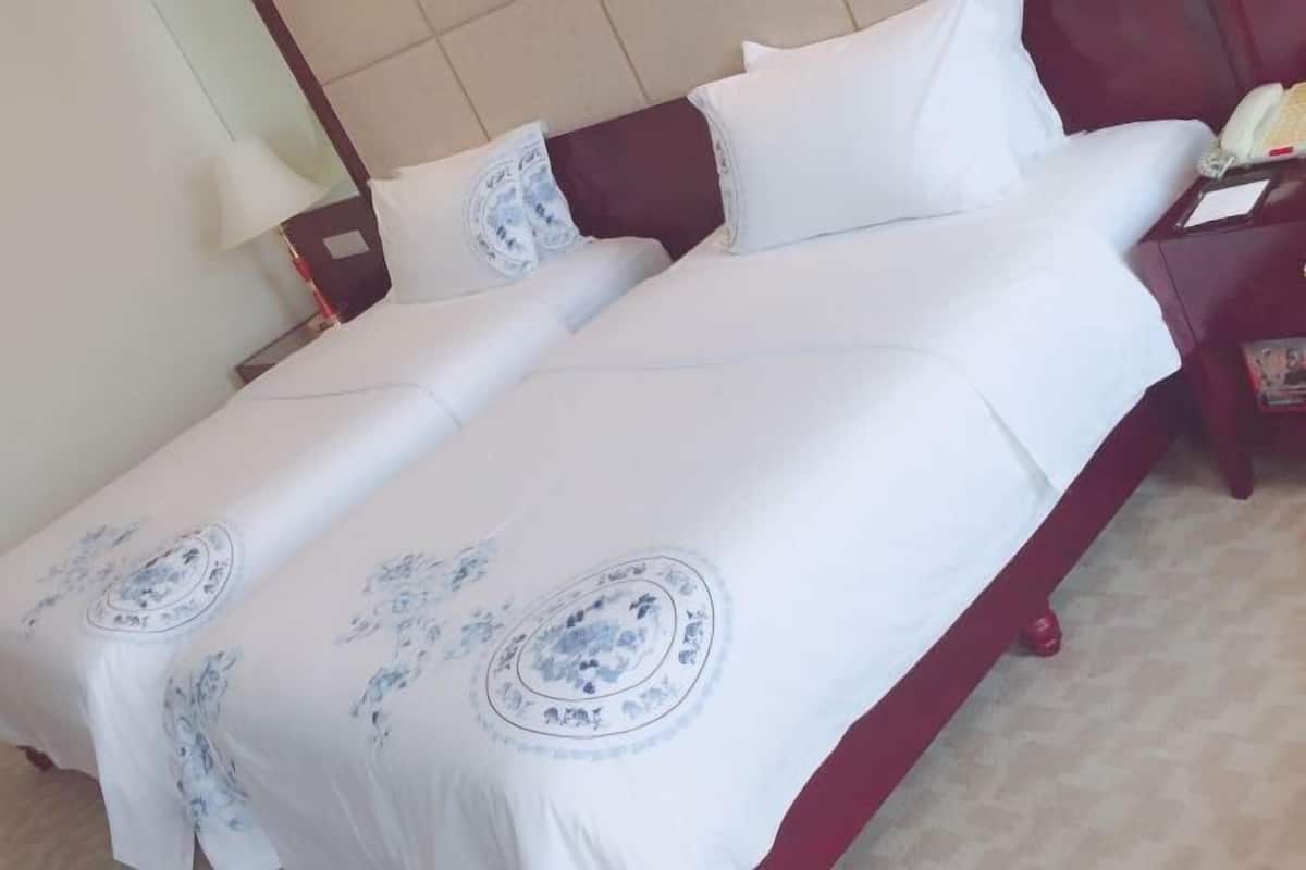 Un lit double avec une literie blanche et des motifs floraux bleus, une table de chevet avec une lampe et un téléphone.