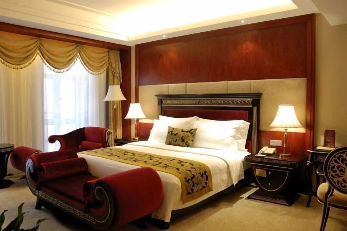 Une chambre d’hôtel avec un grand lit, deux tables de chevet avec des lampes, un fauteuil rouge et une tête de lit en bois.