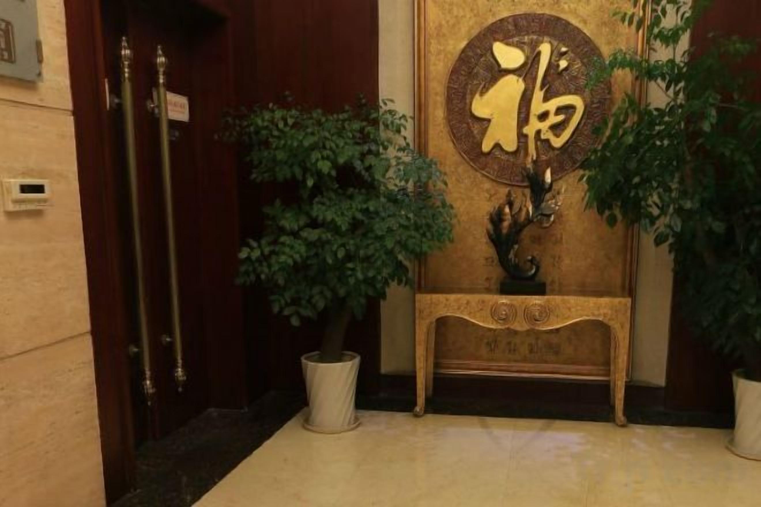 A reception area with a wooden door, a potted plant, and a decorative console table with a gold emblem.