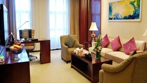Una habitación de hotel con un escritorio, un sofá, un televisor y un cuadro en la pared.