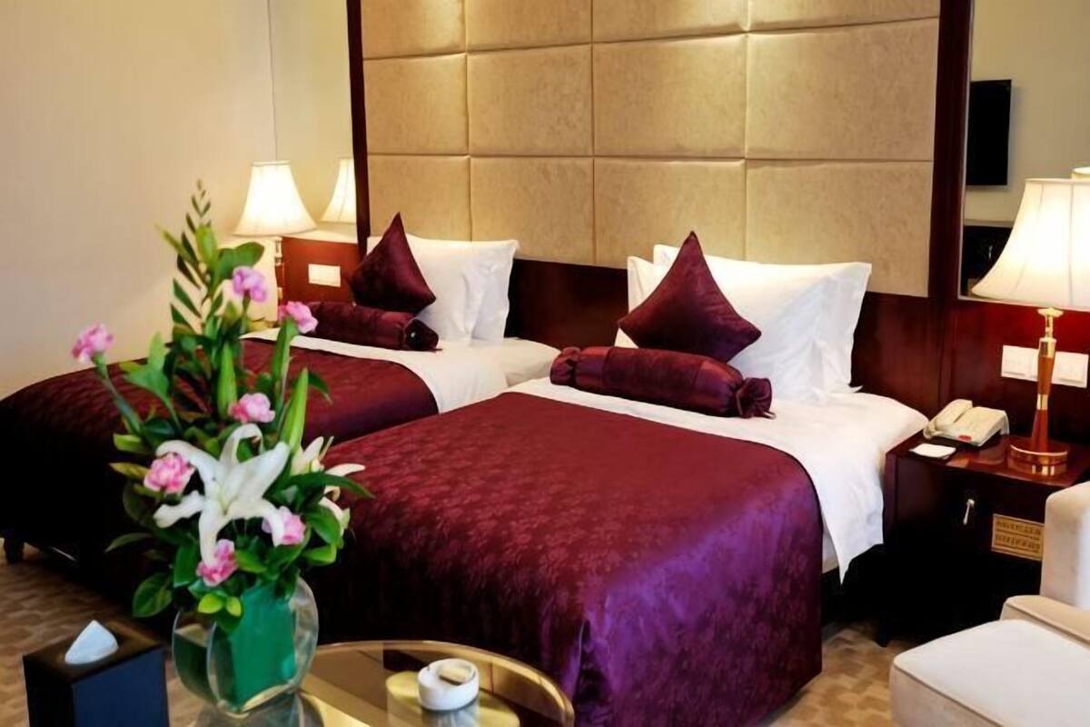 Une chambre d’hôtel avec deux lits, une table de chevet avec une lampe, un vase avec des fleurs et une petite table avec une tasse.