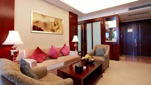 Un vestíbulo de hotel con sofá, sillones, una mesa de centro, un cuadro y un mostrador de recepción.