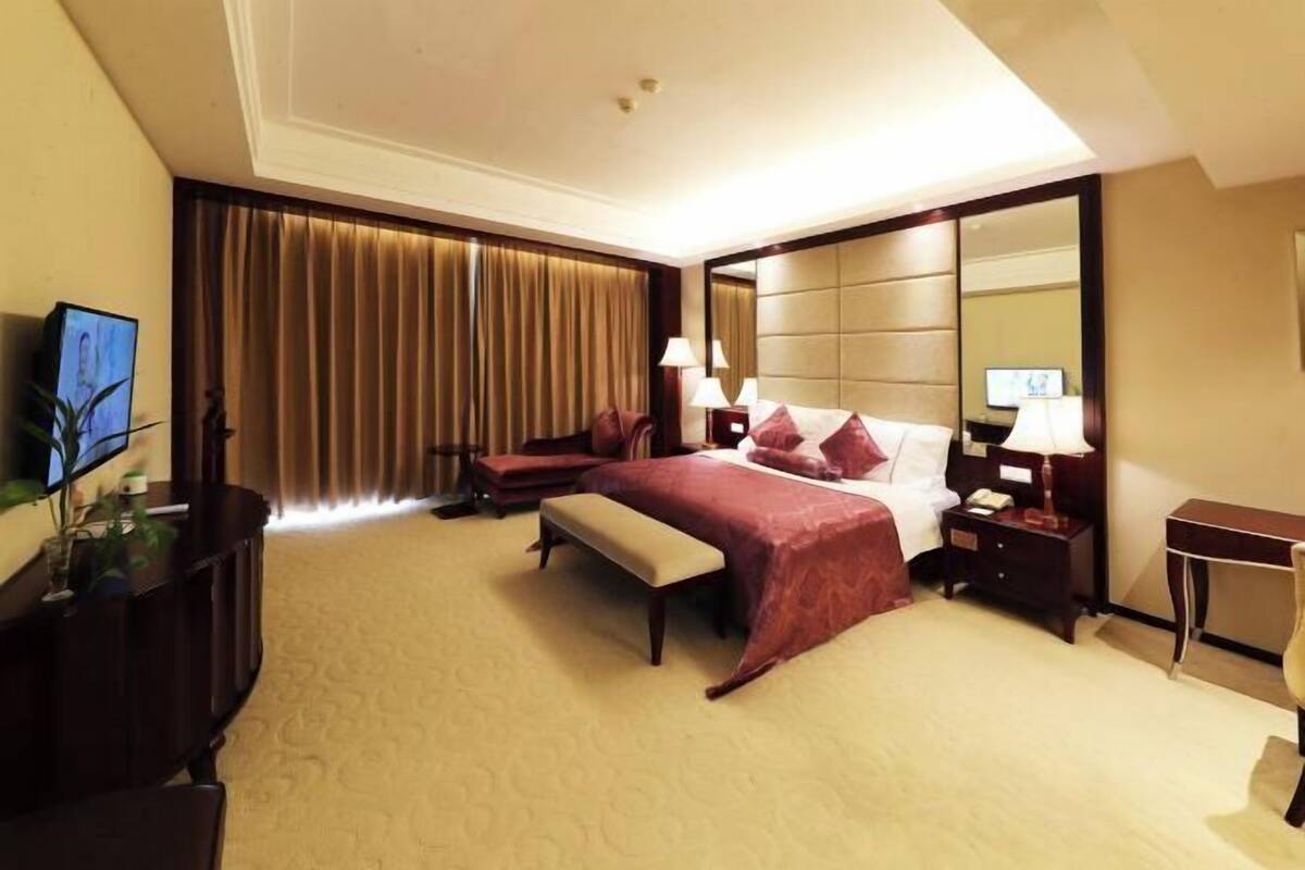 Une chambre d’hôtel avec un grand lit, un bureau, une télévision et une grande fenêtre avec des rideaux.