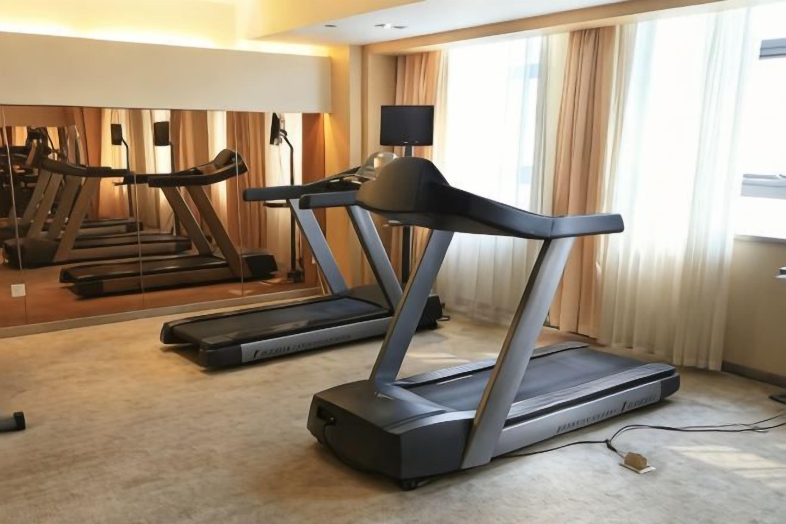 A hotel room with a treadmill, a large mirror, and a view of the outdoors.